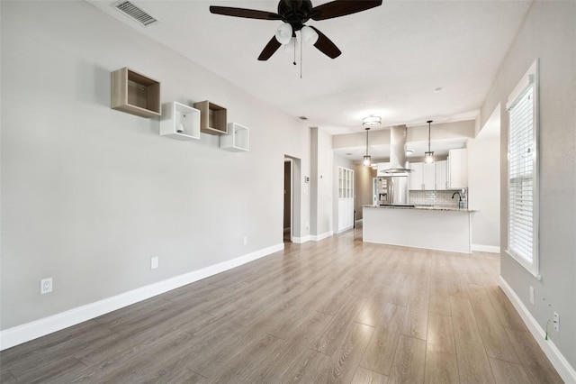 unfurnished living room featuring light hardwood / wood-style floors, ceiling fan, and sink