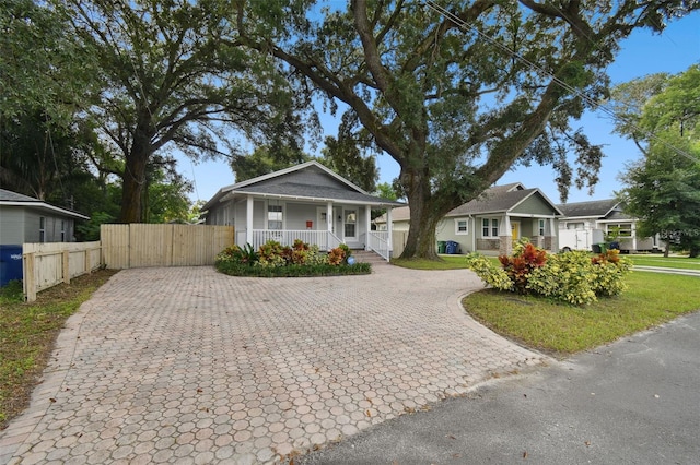 bungalow featuring decorative driveway, covered porch, fence, and a gate