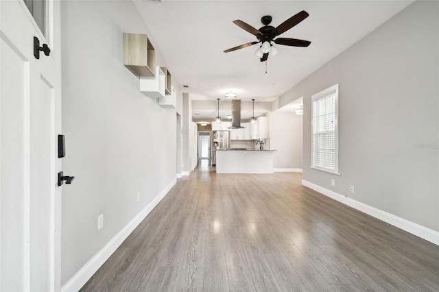 unfurnished living room with ceiling fan, baseboards, and wood finished floors