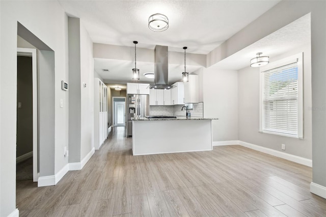 kitchen with island range hood, white cabinets, decorative backsplash, light wood-style flooring, and light stone countertops