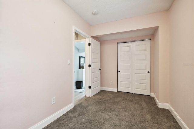 unfurnished bedroom with a closet, dark carpet, and baseboards