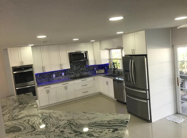 kitchen with sink, tasteful backsplash, white cabinetry, appliances with stainless steel finishes, and dark stone countertops