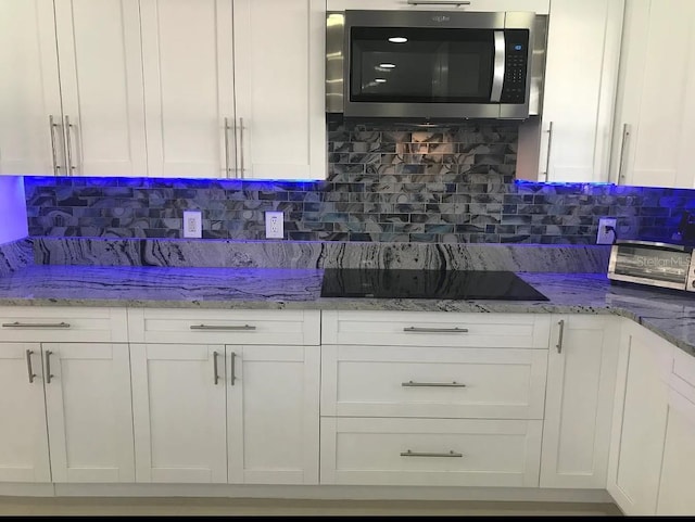 kitchen featuring light stone counters, black electric cooktop, tasteful backsplash, and white cabinetry