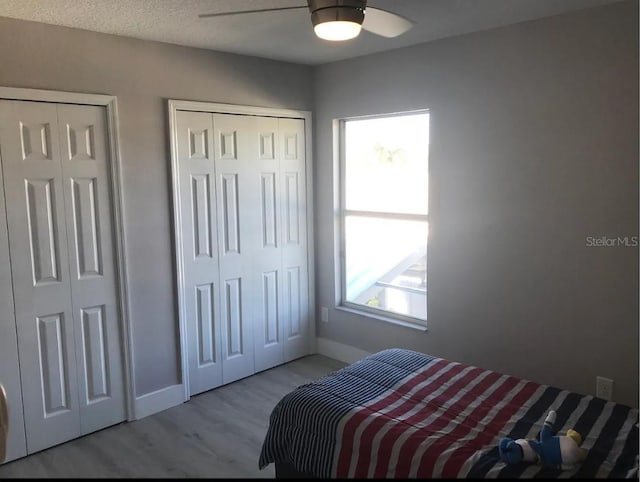 bedroom featuring light hardwood / wood-style floors, ceiling fan, multiple closets, and a textured ceiling