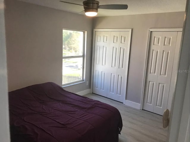 bedroom featuring light wood-type flooring, multiple closets, and ceiling fan