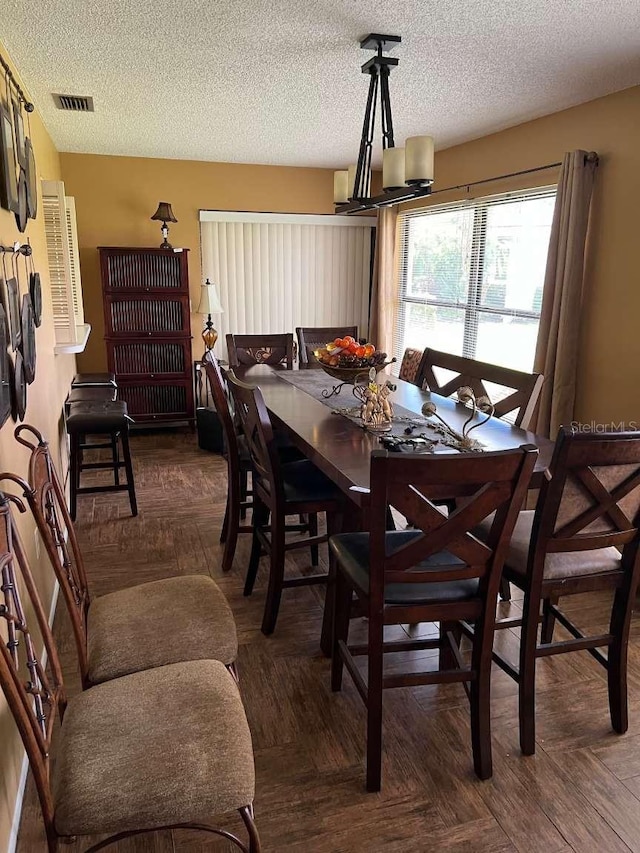 dining space featuring a textured ceiling, a notable chandelier, and dark parquet flooring