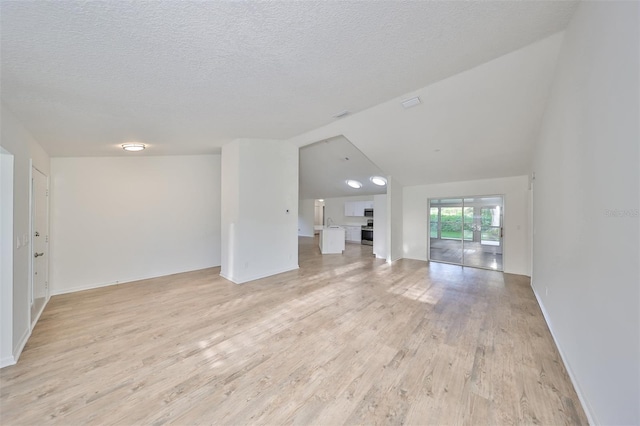 unfurnished living room with vaulted ceiling, light hardwood / wood-style flooring, and a textured ceiling