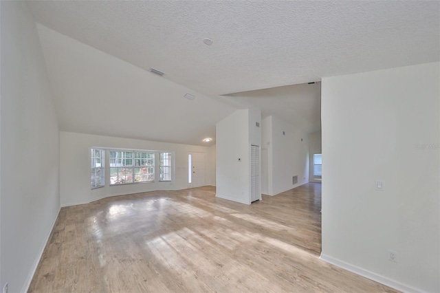 unfurnished living room with a textured ceiling, light hardwood / wood-style floors, and vaulted ceiling