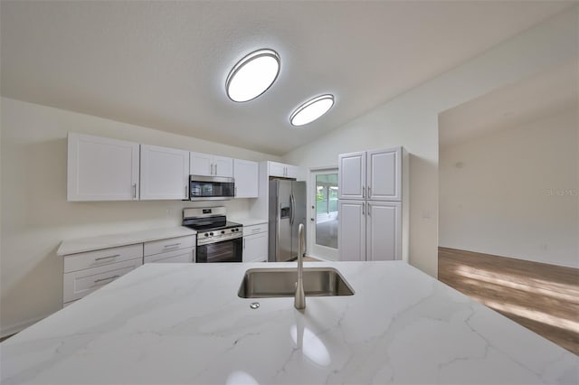 kitchen with light stone countertops, white cabinetry, sink, stainless steel appliances, and lofted ceiling