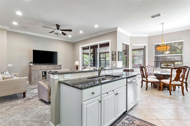 kitchen featuring dark stone countertops, pendant lighting, an island with sink, sink, and ceiling fan