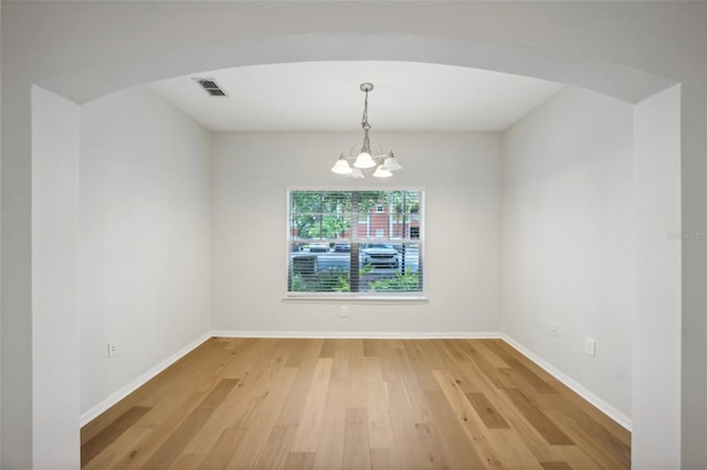 unfurnished room with visible vents, light wood finished floors, baseboards, arched walkways, and a chandelier