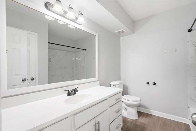 bathroom with toilet, hardwood / wood-style flooring, vanity, and tiled shower