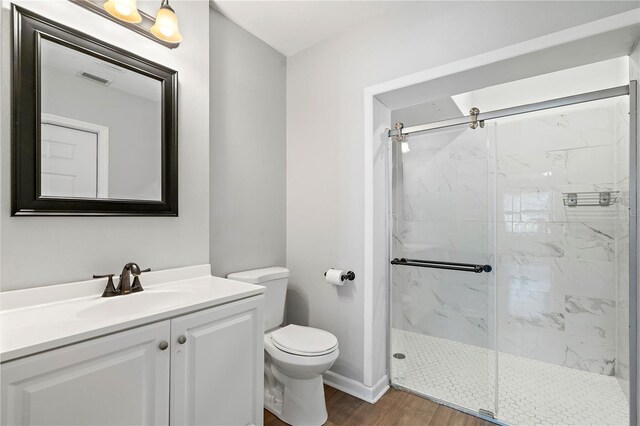 bathroom featuring wood-type flooring, vanity, toilet, and a shower with shower door