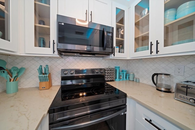 kitchen featuring white cabinets, black electric range, light stone countertops, and decorative backsplash