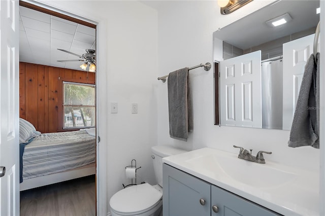 bathroom featuring wood-type flooring, wood walls, ceiling fan, vanity, and toilet