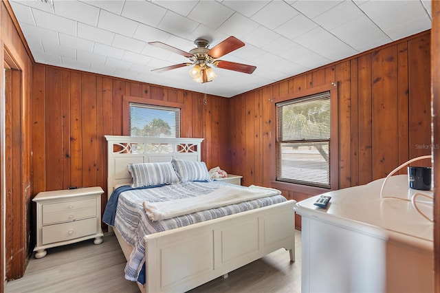 bedroom with light hardwood / wood-style floors, wooden walls, and ceiling fan