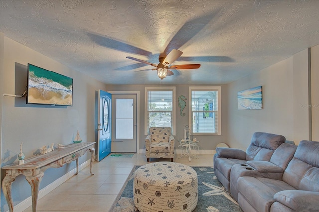 living area featuring light tile patterned floors, a ceiling fan, baseboards, and a textured ceiling