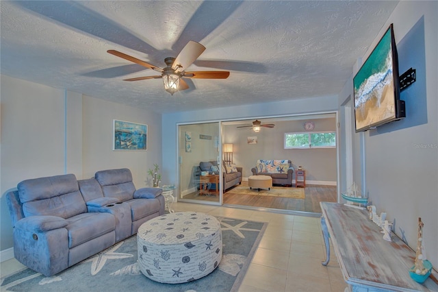 living area with light tile patterned flooring, baseboards, a textured ceiling, and ceiling fan