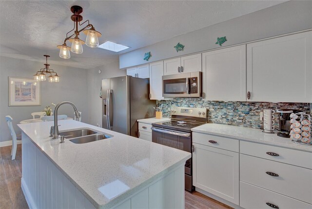 kitchen featuring a skylight, decorative light fixtures, stainless steel appliances, sink, and a kitchen island with sink