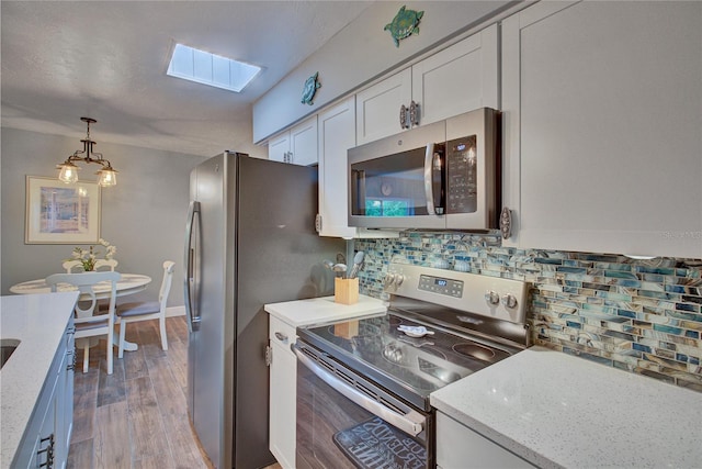 kitchen with appliances with stainless steel finishes, decorative backsplash, white cabinetry, a skylight, and light wood-type flooring