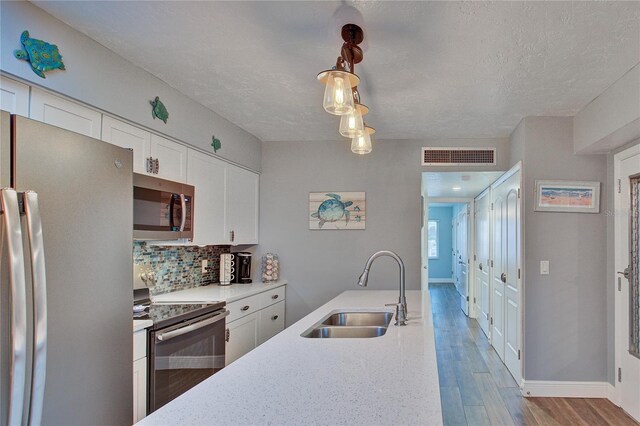 kitchen with light wood-type flooring, appliances with stainless steel finishes, white cabinetry, sink, and pendant lighting