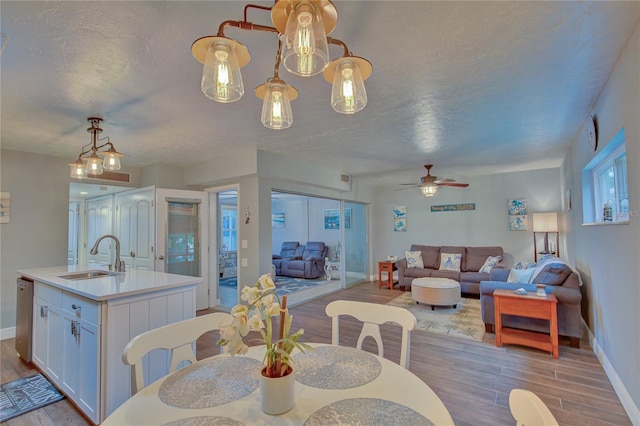 dining area with a textured ceiling, sink, ceiling fan with notable chandelier, and light hardwood / wood-style floors