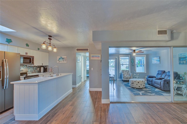 kitchen with stainless steel appliances, ceiling fan, hanging light fixtures, hardwood / wood-style flooring, and white cabinets