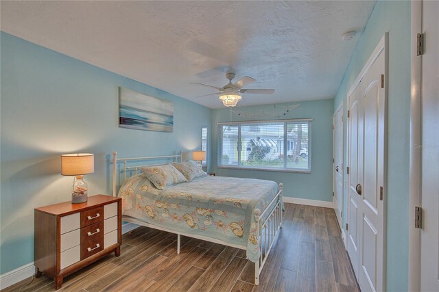 bedroom with a textured ceiling, dark wood-type flooring, ceiling fan, and a closet