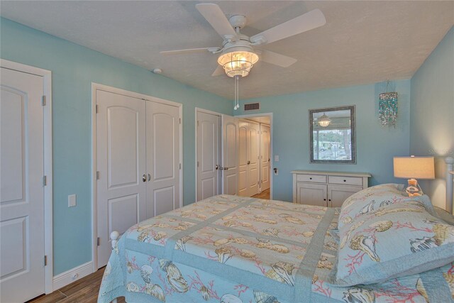 bedroom with multiple closets, hardwood / wood-style flooring, and ceiling fan