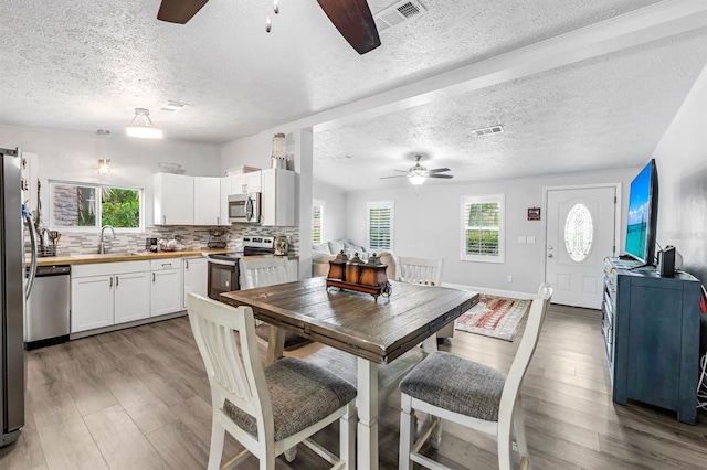 dining space with light wood-type flooring, ceiling fan, and a textured ceiling