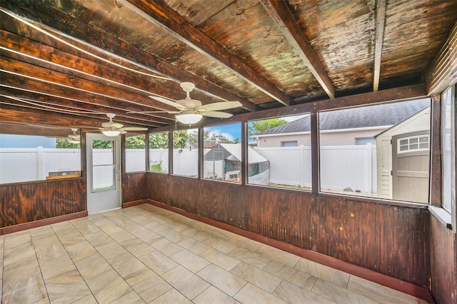 unfurnished sunroom featuring beamed ceiling and ceiling fan