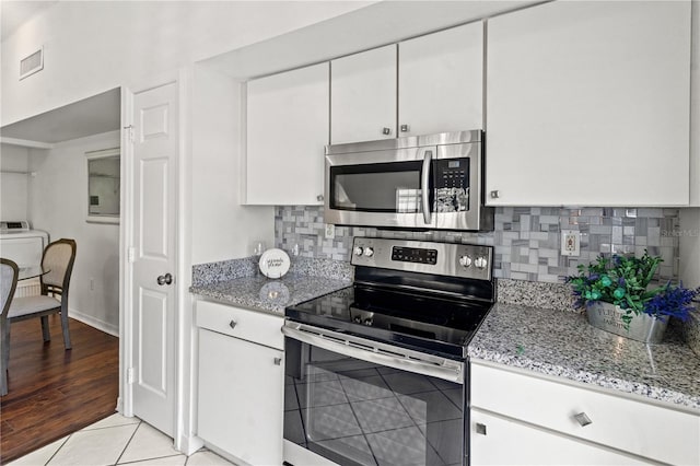 kitchen featuring appliances with stainless steel finishes, washer / dryer, backsplash, white cabinets, and light stone counters