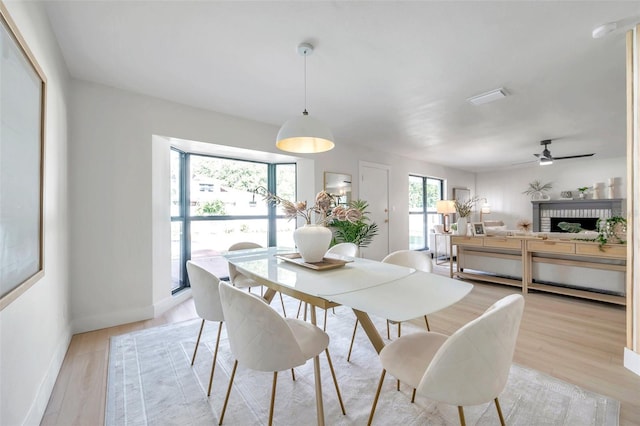 dining area featuring ceiling fan, light hardwood / wood-style floors, and a brick fireplace