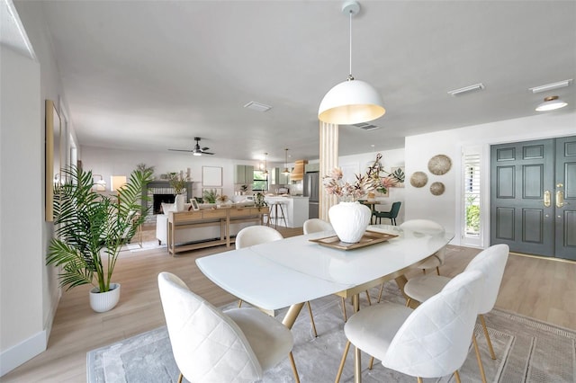 dining space with a fireplace, light hardwood / wood-style flooring, and ceiling fan