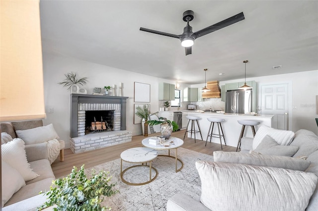 living room featuring a brick fireplace, sink, ceiling fan, and light hardwood / wood-style floors