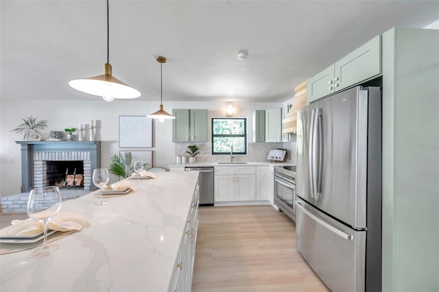 kitchen featuring a brick fireplace, decorative light fixtures, light wood-type flooring, light stone counters, and stainless steel appliances