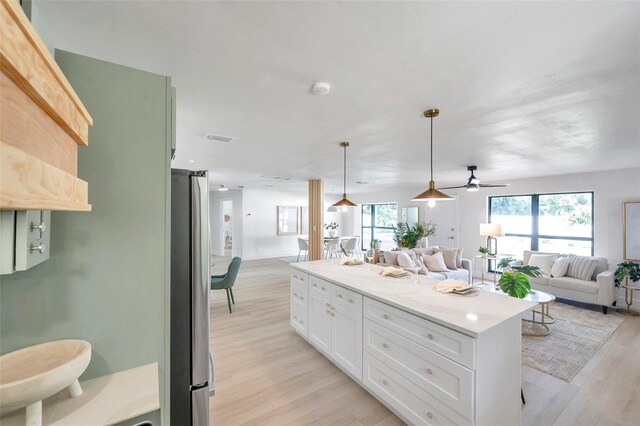 kitchen with white cabinets, a center island, light wood-type flooring, stainless steel refrigerator, and pendant lighting