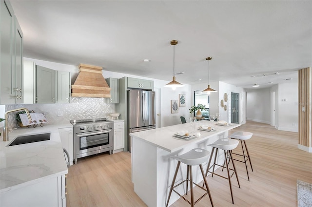 kitchen with light hardwood / wood-style flooring, custom range hood, appliances with stainless steel finishes, hanging light fixtures, and sink