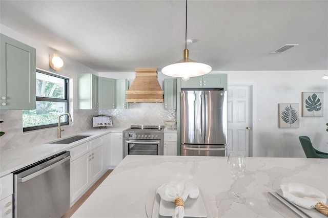 kitchen with custom exhaust hood, green cabinetry, light stone countertops, and stainless steel appliances