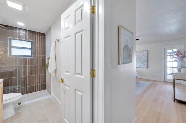 bathroom featuring vanity, hardwood / wood-style floors, a tile shower, tile walls, and toilet