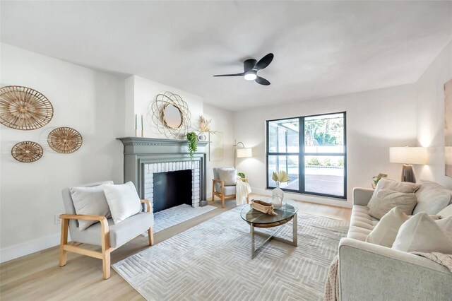 living room with light wood-type flooring, a brick fireplace, and ceiling fan