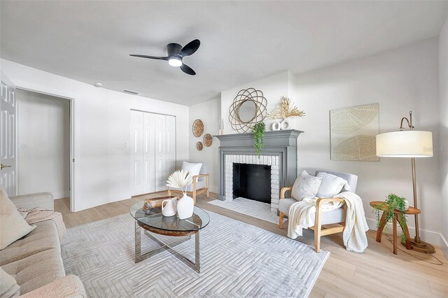 living room with ceiling fan, a brick fireplace, and light hardwood / wood-style floors