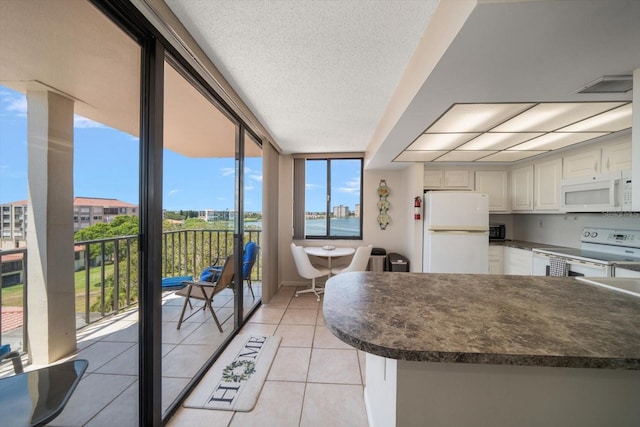 kitchen featuring expansive windows, light tile patterned floors, a textured ceiling, and white appliances