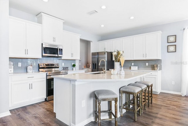 kitchen featuring a breakfast bar area, an island with sink, white cabinets, appliances with stainless steel finishes, and dark hardwood / wood-style flooring