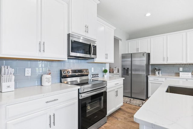 kitchen with sink, light hardwood / wood-style flooring, backsplash, white cabinetry, and stainless steel appliances