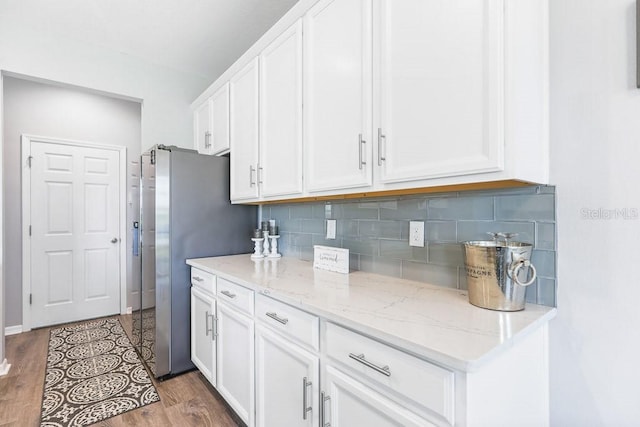 kitchen featuring light stone counters, white cabinets, decorative backsplash, hardwood / wood-style floors, and stainless steel fridge