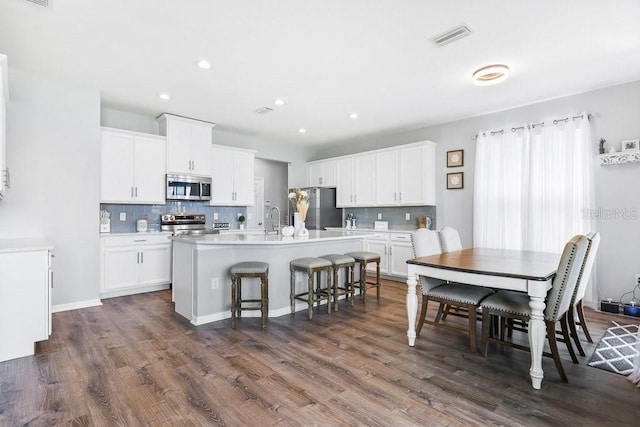 kitchen with white cabinets, a kitchen island with sink, stainless steel appliances, dark hardwood / wood-style floors, and a kitchen breakfast bar