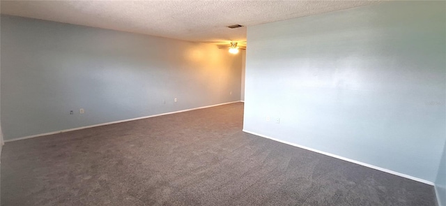 empty room featuring a textured ceiling, dark carpet, and ceiling fan