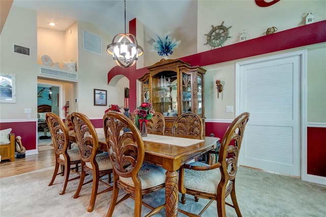 dining area featuring visible vents, light carpet, high vaulted ceiling, and an inviting chandelier