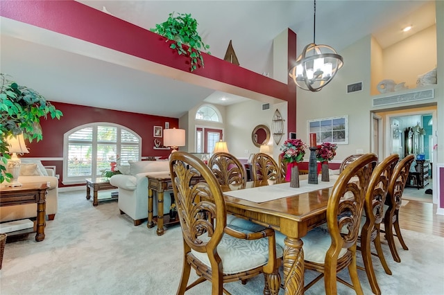 dining space featuring a notable chandelier, visible vents, light colored carpet, and high vaulted ceiling